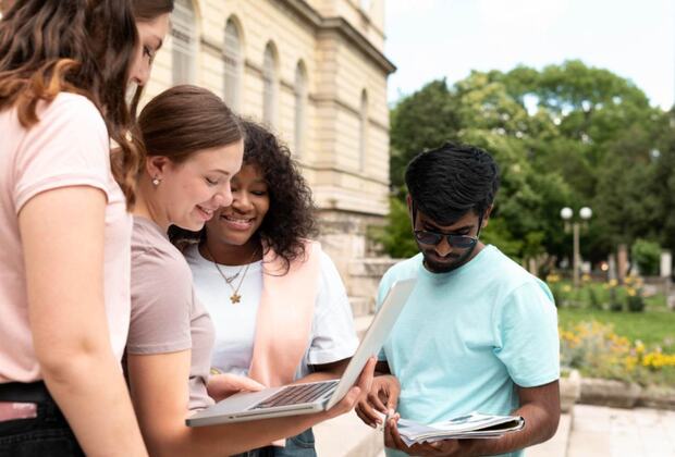 Students reviewing course information on a laptop outside a university building